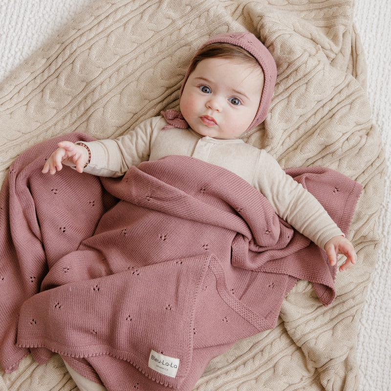 Baby resting on Bleu La La Organic Pointelle Luxury Knit Swaddle Blanket in sugar plum for soft all-season warmth.