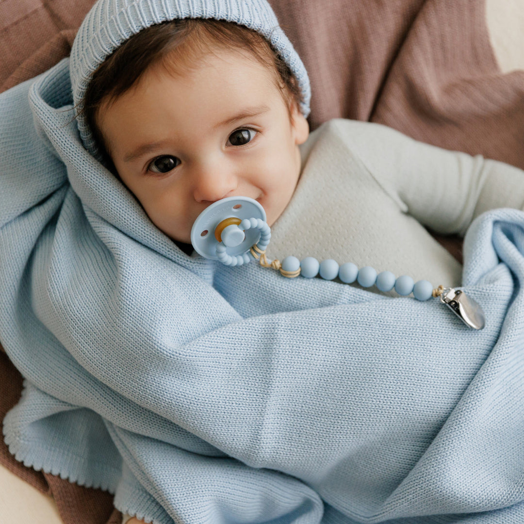 Baby wrapped in a Bleu La La light blue organic knit blanket with pacifier, cozy breathable cotton