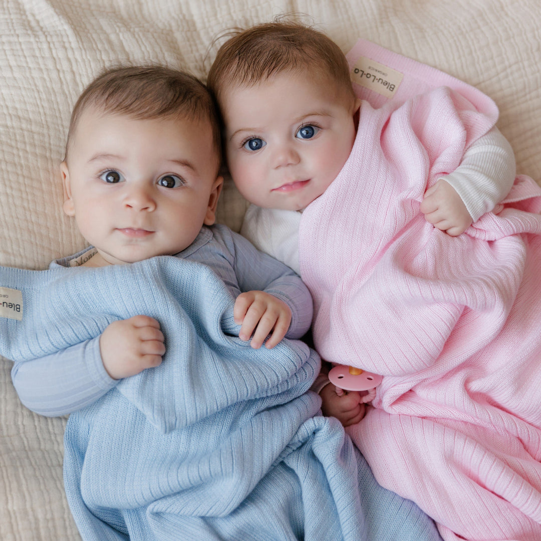Two babies wrapped in Bleu La La Organic Ribbed Knit Cotton Baby Blankets in blue and pink, soft breathable knitted baby swaddles for newborn comfort