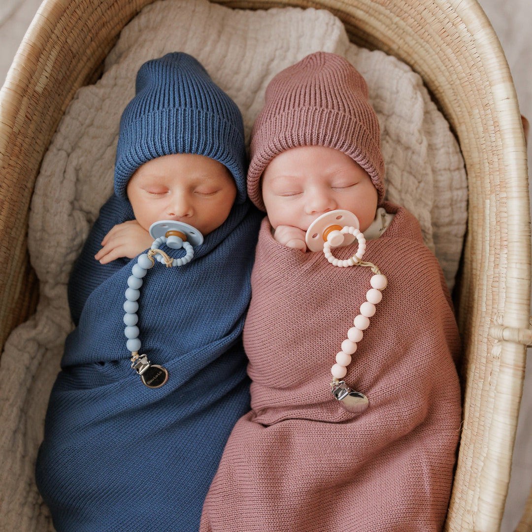 Two babies wrapped in Bleu La La knit blankets, navy and mauve, matching hats and pacifiers