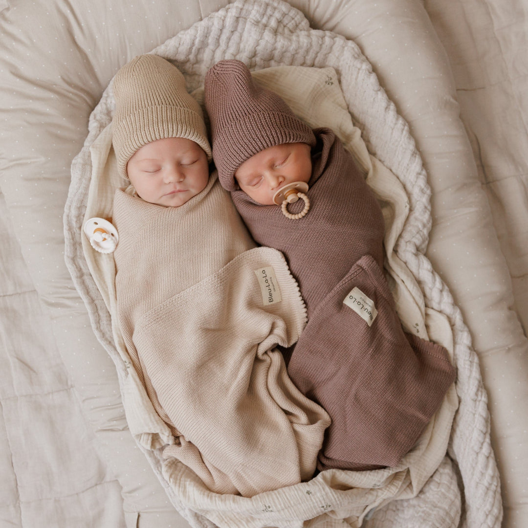 Two babies snuggled in Bleu La La organic cotton knit blankets, one beige and one brown, cozy newborn set