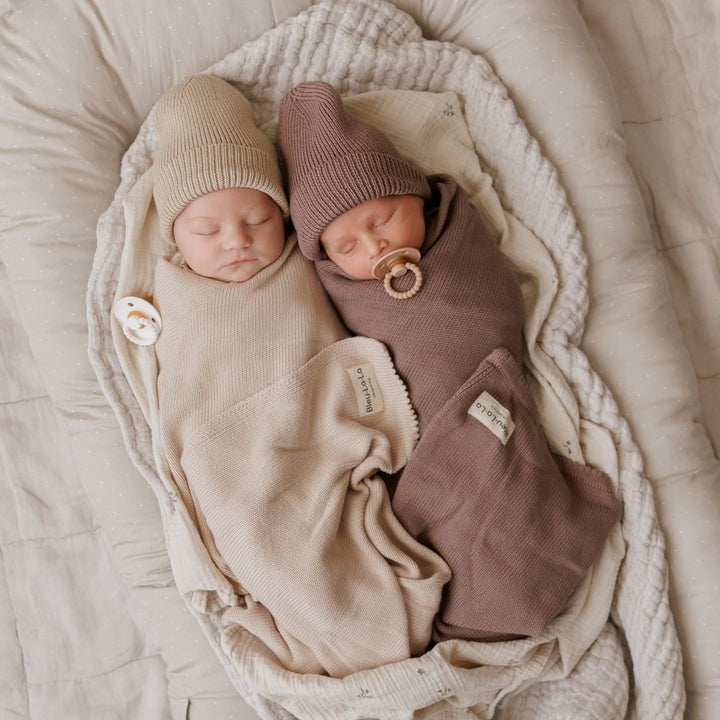 Two babies snuggled in Bleu La La organic cotton knit blankets, one beige and one brown, cozy newborn set