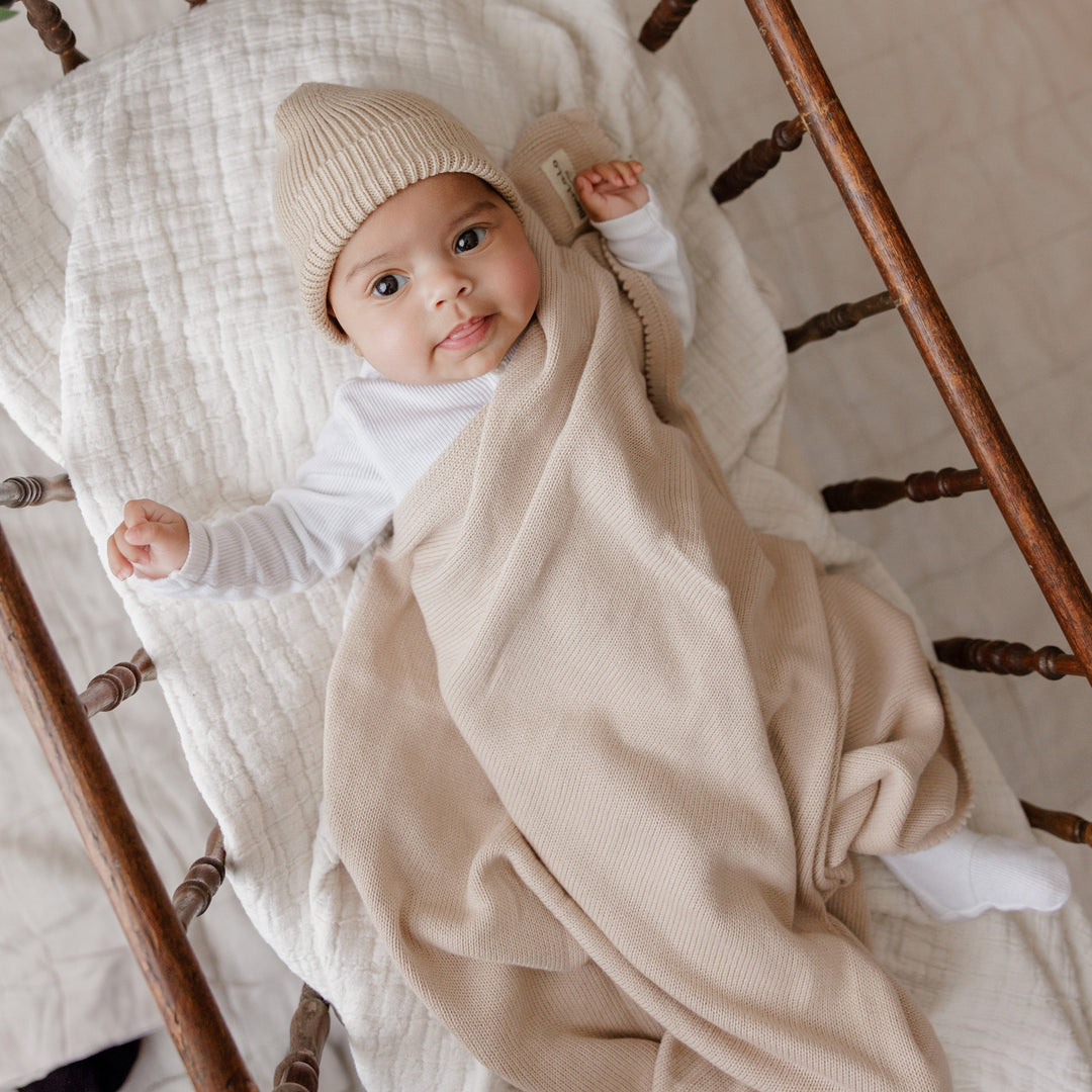 Baby wrapped in a Bleu La La beige organic knit blanket, soft luxe newborn styling