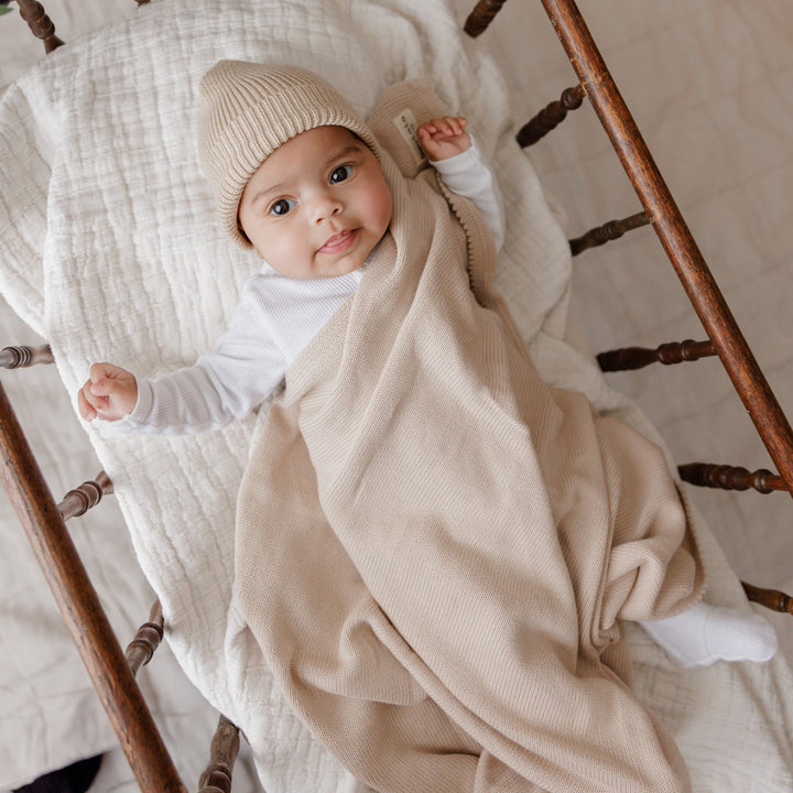 Baby wrapped in a Bleu La La beige organic knit blanket, soft luxe newborn styling