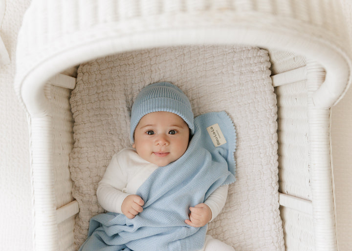 Baby in a bassinet wrapped in a Bleu La La light blue organic knit blanket, breathable for sleep