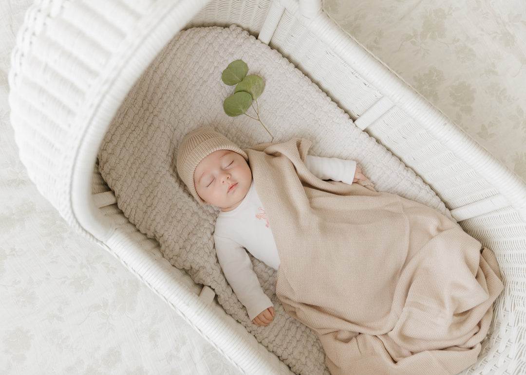 Newborn in a bassinet wrapped in a Bleu La La beige organic knit blanket, soft luxe baby comfort