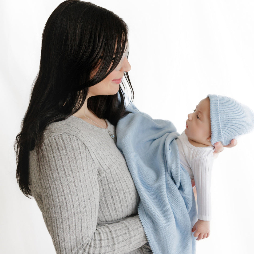 Mom holding baby wrapped in a Bleu La La light blue organic knit blanket, soft cotton cuddle moment