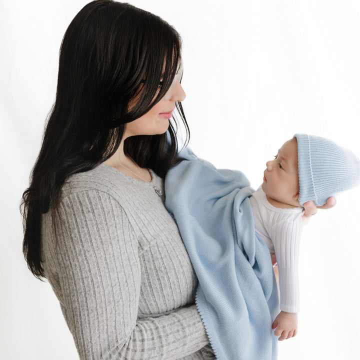 Mom holding baby wrapped in a Bleu La La light blue organic knit blanket, soft cotton cuddle moment