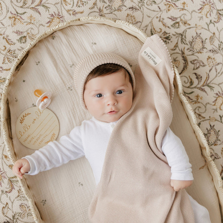 Baby lying in a Bleu La La beige organic knit blanket, luxe newborn wrap with arms up