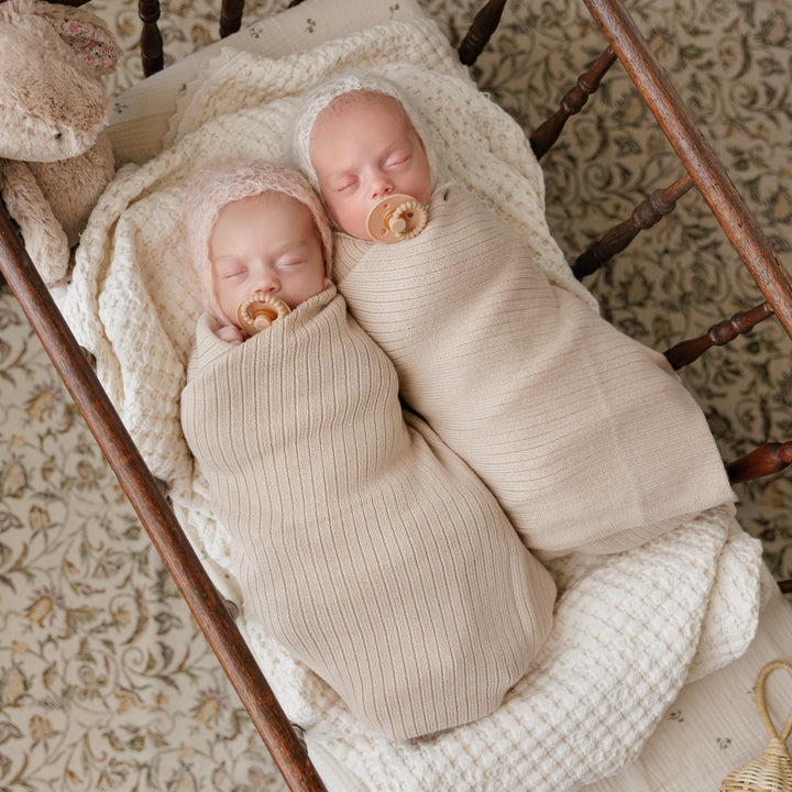 Baby wrapped in blush pink Bleu La La Organic Ribbed Knit Cotton Baby Blanket on textured bedding, soft ribbed baby swaddle