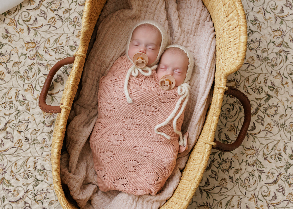 Newborn wrapped in Bleu La La 100% Cotton Luxury Knit Heart Swaddle Baby Blanket in Rose Pink inside a bassinet for cozy sleep.