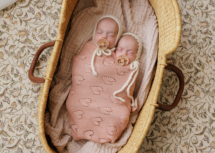 Newborn wrapped in Bleu La La 100% Cotton Luxury Knit Heart Swaddle Baby Blanket in Rose Pink inside a bassinet for cozy sleep.