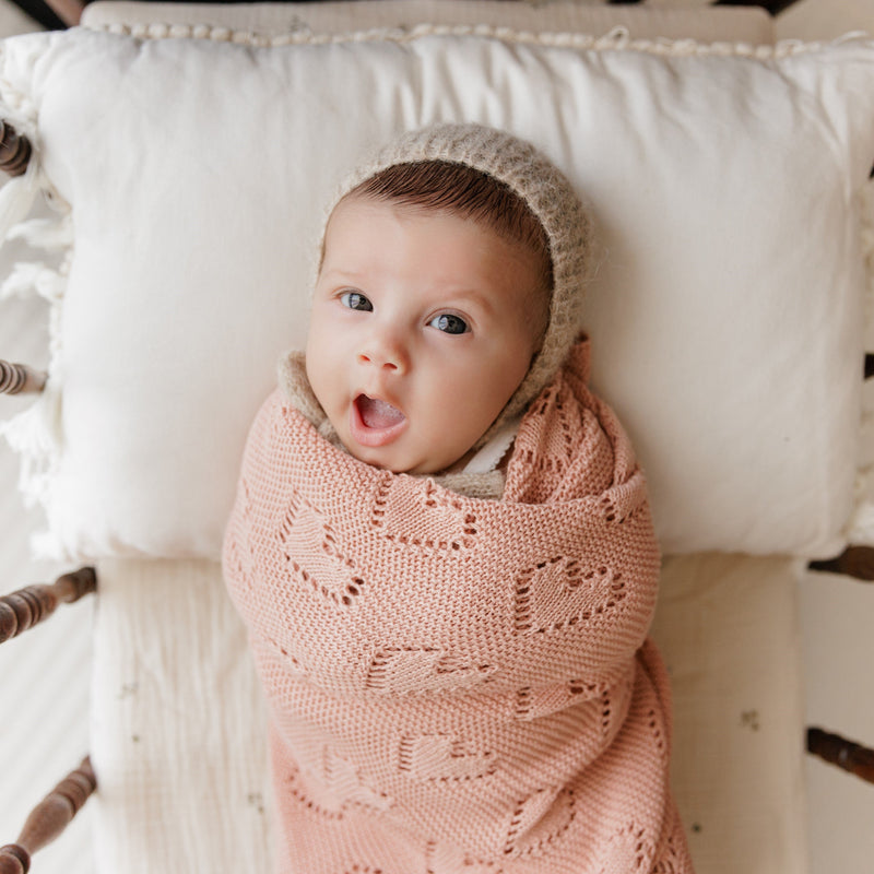 Baby swaddled in Bleu La La 100% Cotton Luxury Knit Heart Swaddle Baby Blanket in rose pink on a soft pillow for breathable comfort.