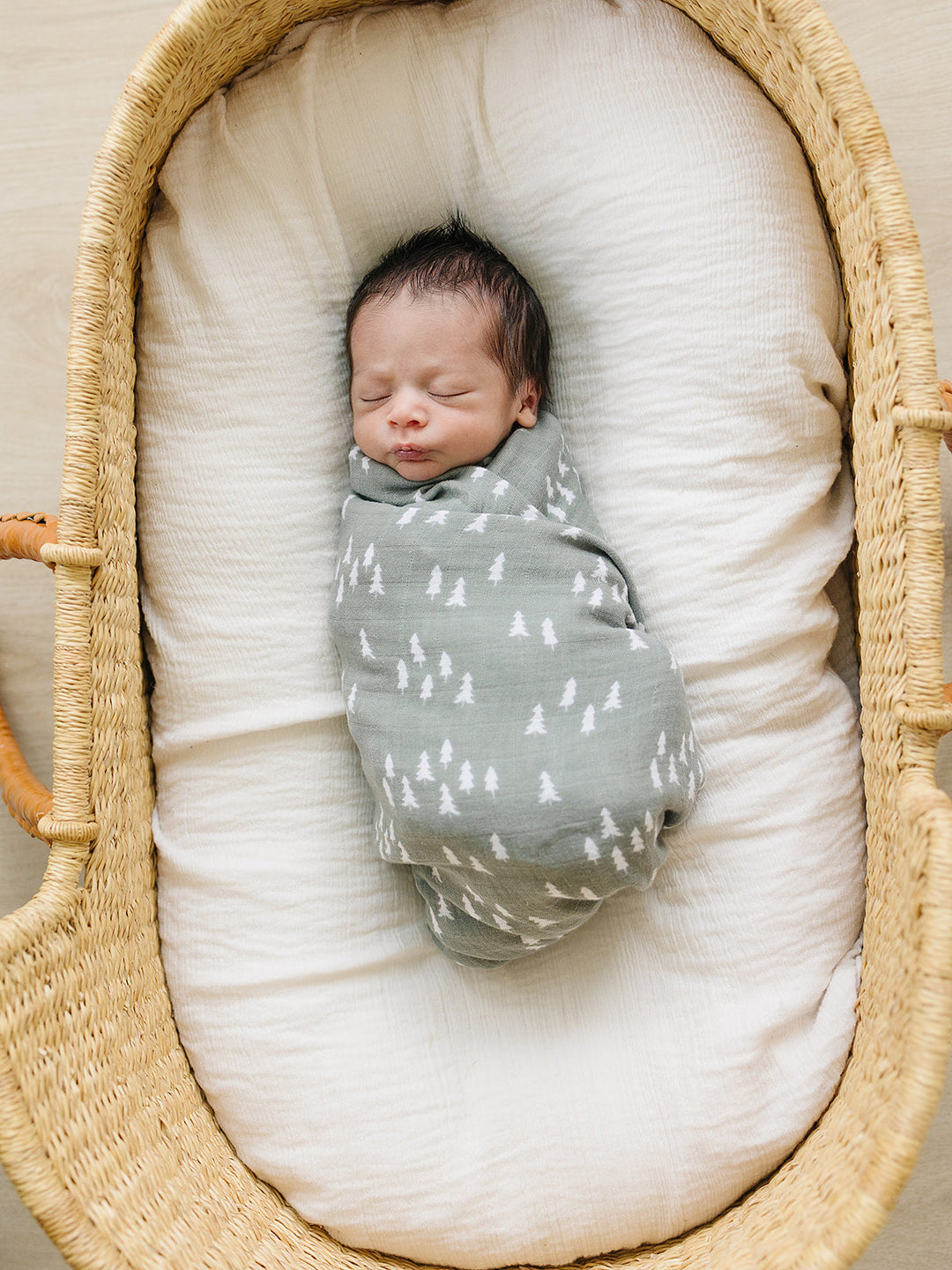 Pines Muslin Swaddle Blanket draped over a crib rail, a breathable bamboo swaddle blanket for newborns.