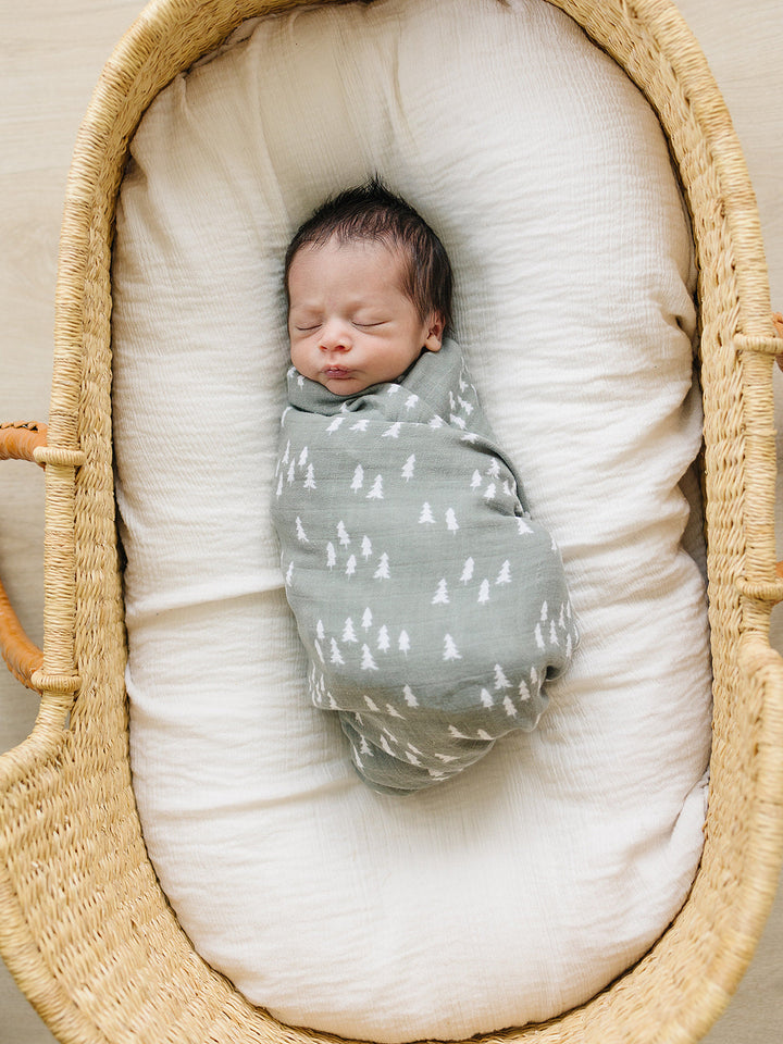 Pines Muslin Swaddle Blanket draped over a crib rail, a breathable bamboo swaddle blanket for newborns.
