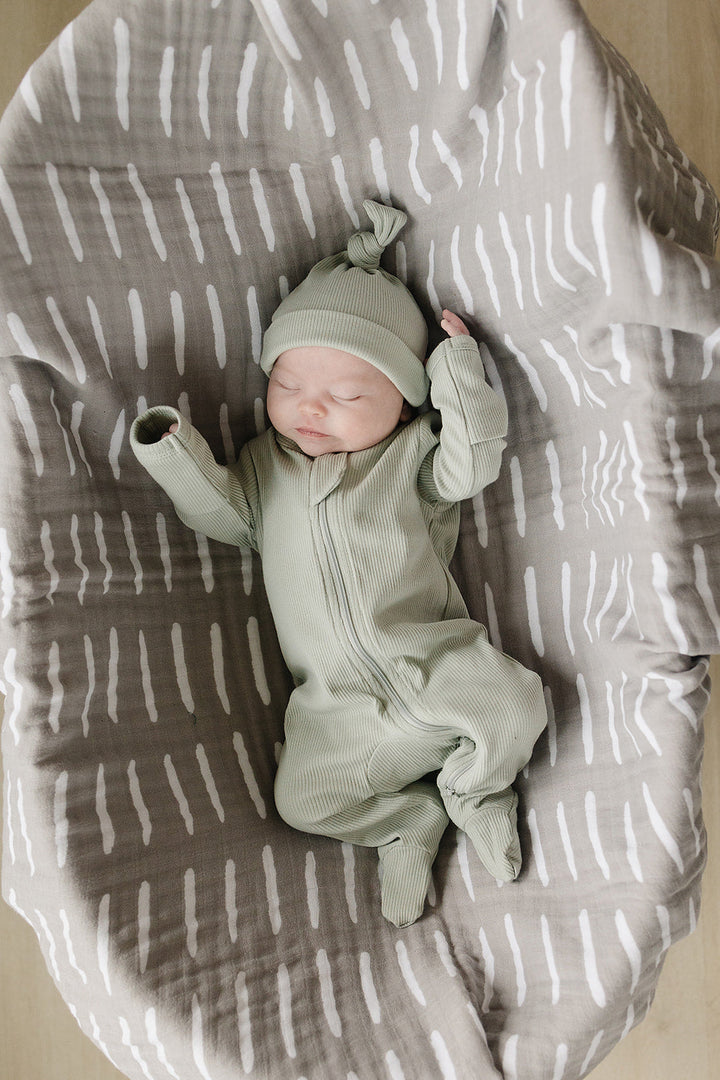 Sage Organic Cotton Ribbed Zipper folded next to a stuffed toy, an organic cotton footie pajama for babies.