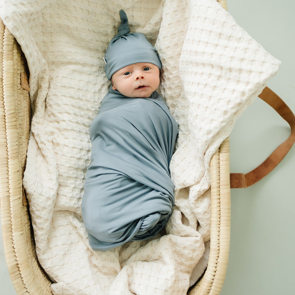 Wrapped around a sleeping newborn, the Dusty Blue Bamboo Stretch Swaddle from Mebie Baby.