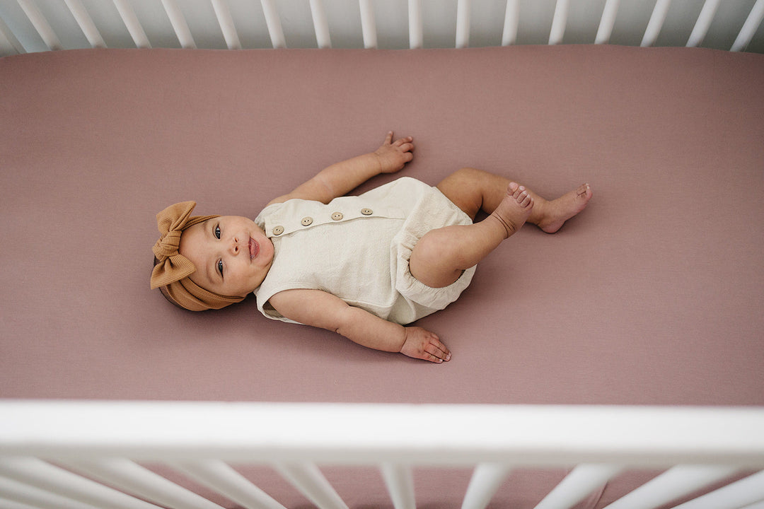 Folded on a nursery shelf, the Dusty Rose Bamboo Stretch Crib Sheet from Mebie Baby.