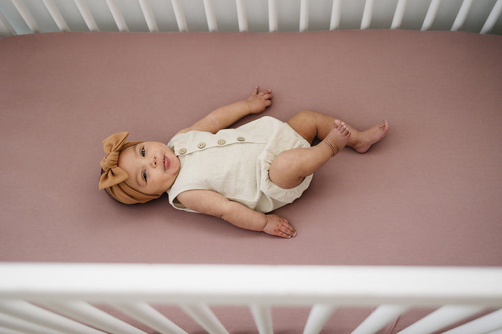 Folded on a nursery shelf, the Dusty Rose Bamboo Stretch Crib Sheet from Mebie Baby.