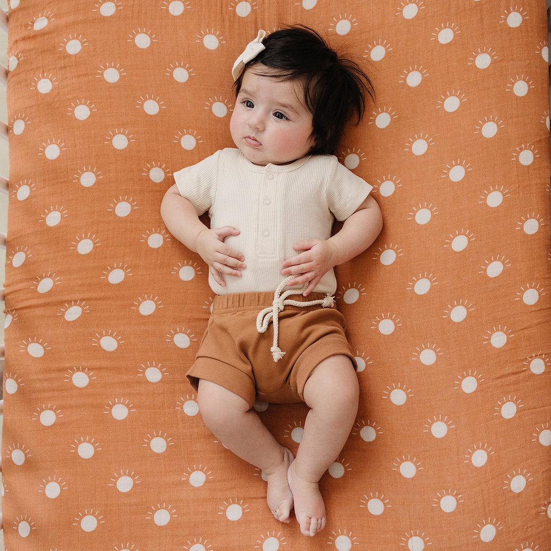 Vanilla Organic Cotton Ribbed Snap Bodysuit folded on a wooden shelf, an organic cotton ribbed baby bodysuit.