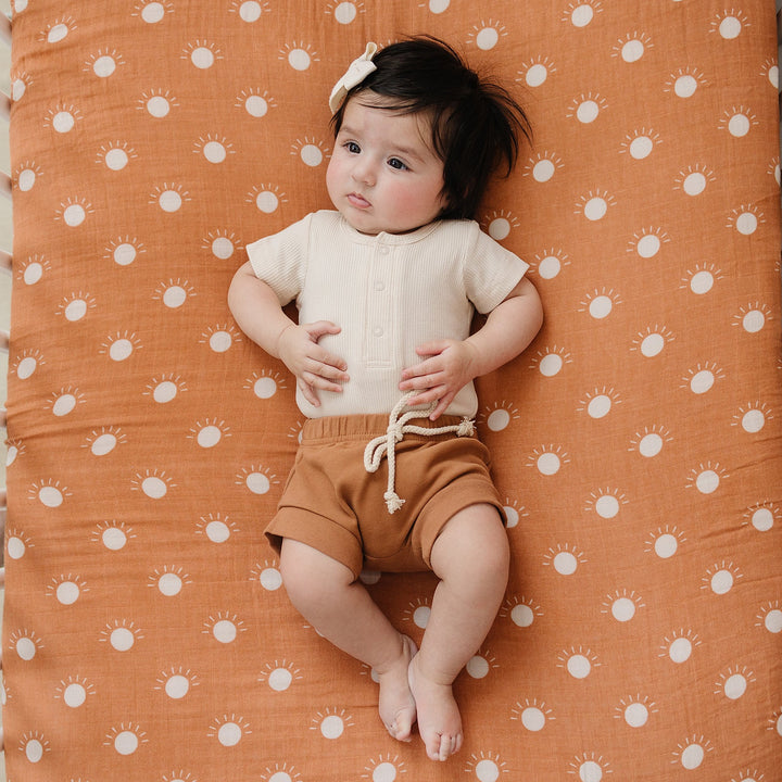 Vanilla Organic Cotton Ribbed Snap Bodysuit folded on a wooden shelf, an organic cotton ribbed baby bodysuit.
