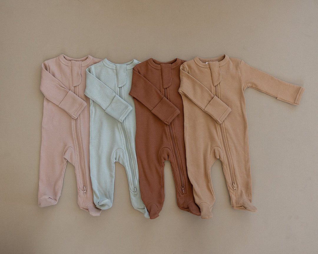 Organic cotton footie pajama for babies, the Pale Pink Organic Cotton Ribbed Zipper zipped up on a smiling infant.
