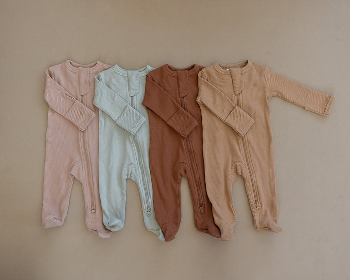 Organic cotton footie pajama for babies, the Pale Pink Organic Cotton Ribbed Zipper zipped up on a smiling infant.