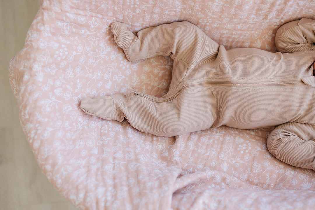 Pale Pink Organic Cotton Ribbed Zipper folded next to a stuffed toy, an organic cotton footie pajama for babies.