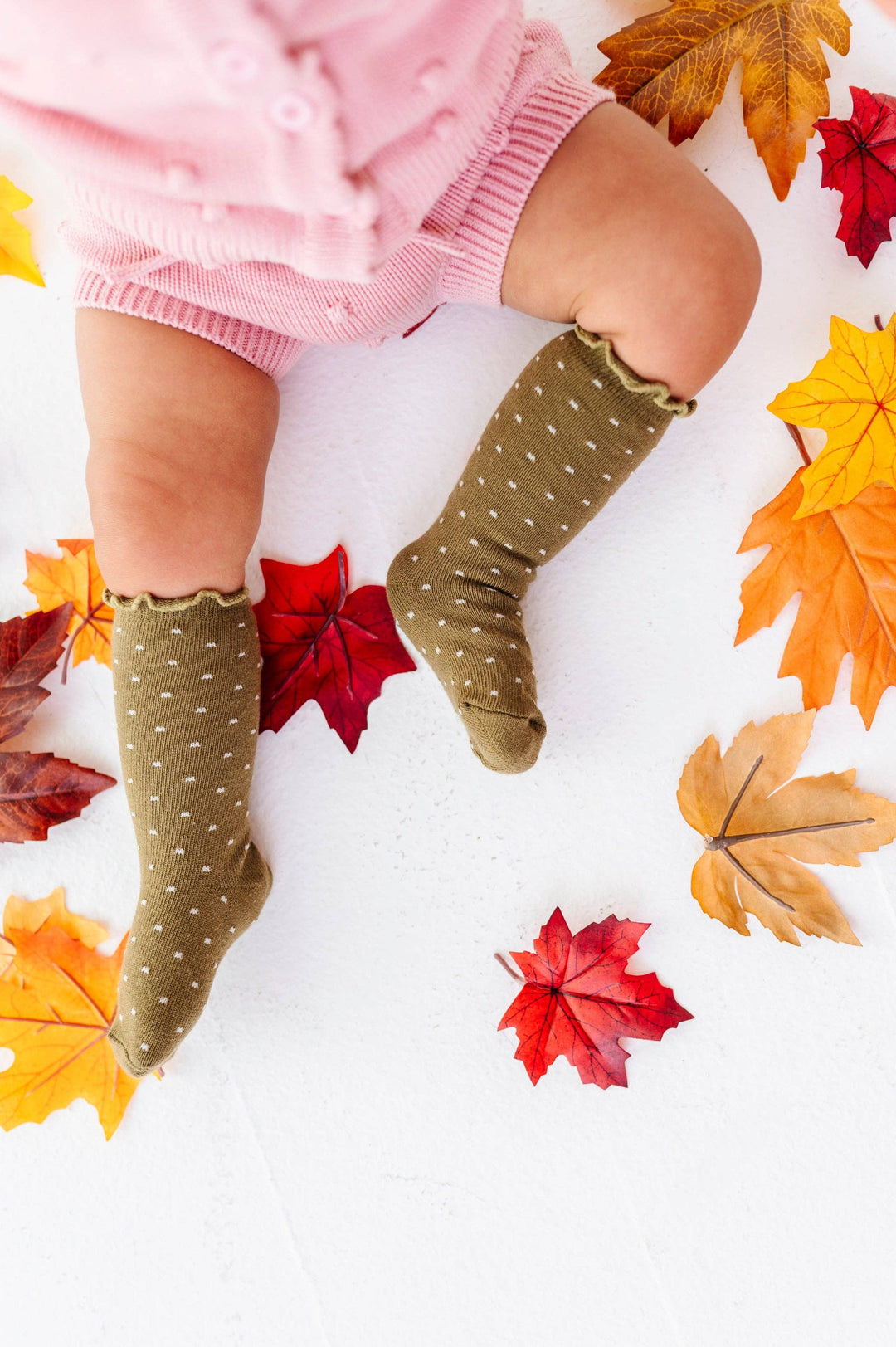 Toddler standing among fall leaves in Little Stocking Co. Dottie Knee Socks in Olive, polka dot baby socks