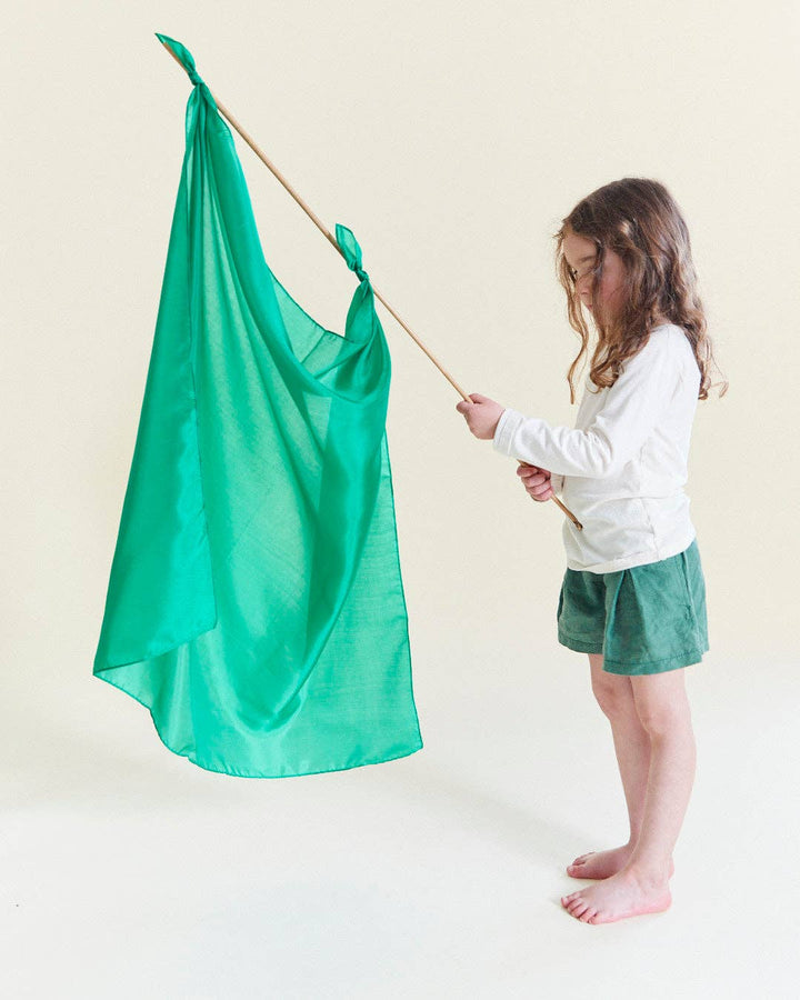 A well loved imaginative toy, children playing with a green Sarah's Silks Solid Color Playsilk like a flag