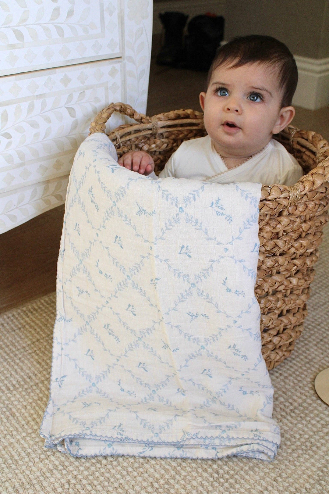 Little Threads muslin blanket held by a baby sitting in a basket showcasing soft texture