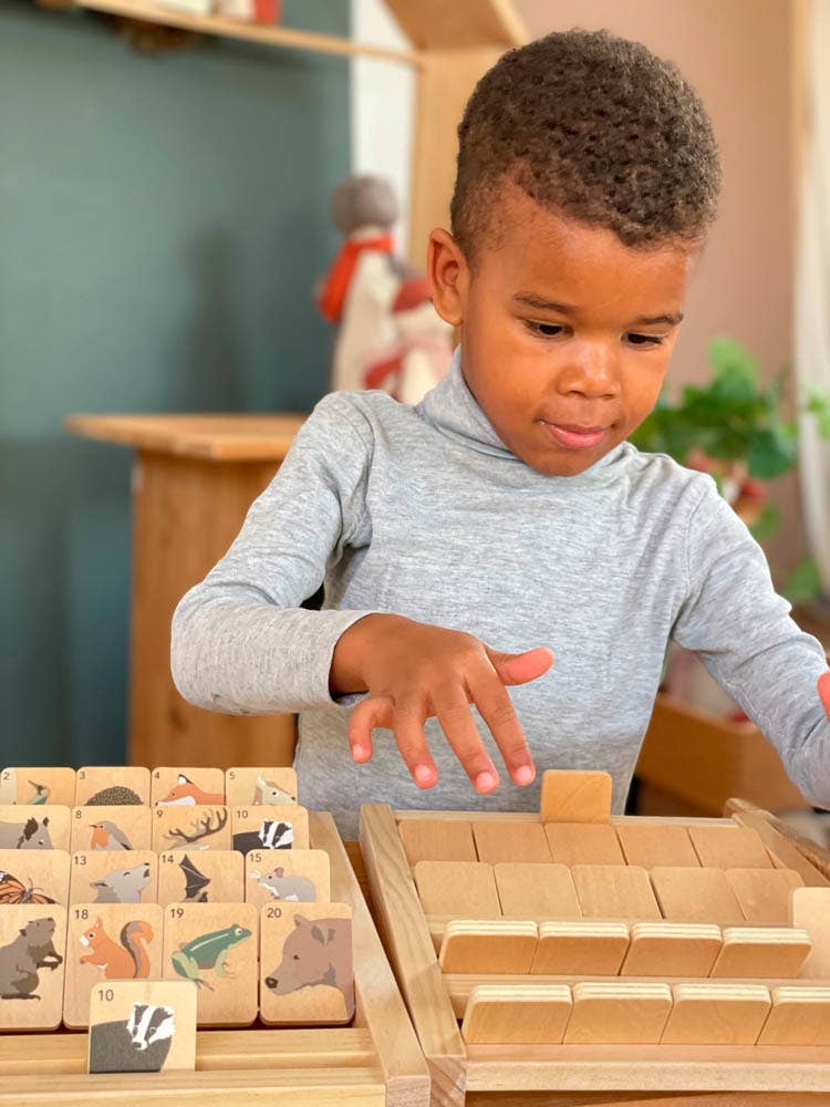 A young child sorts wooden guessing tiles while playing Who Am I, a game made by Egmont