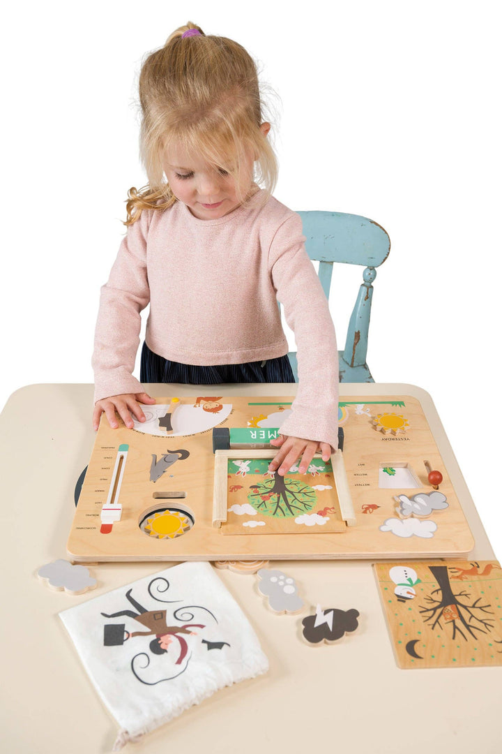 Girl seated at a table arranges pieces on the Weather Watch learning toy by Tender Leaf Toys