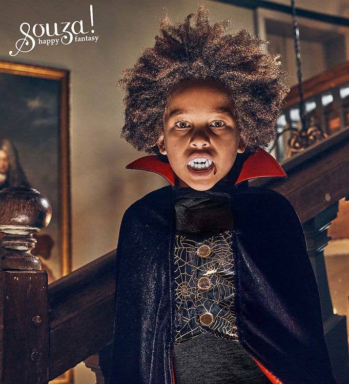 Child in a Souza Dracula costume dark cape and red collar and fake teeth