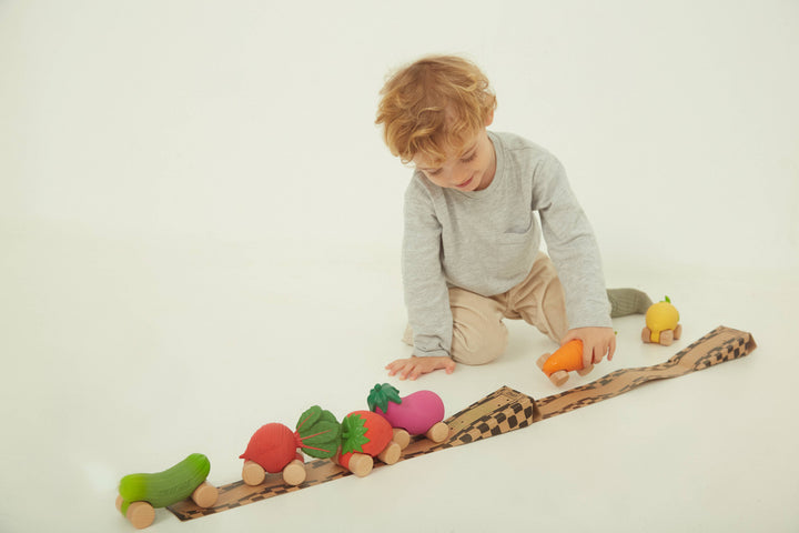 A young boy rolls his Sweetie the Strawberry Baby Car down a wooden ramp track