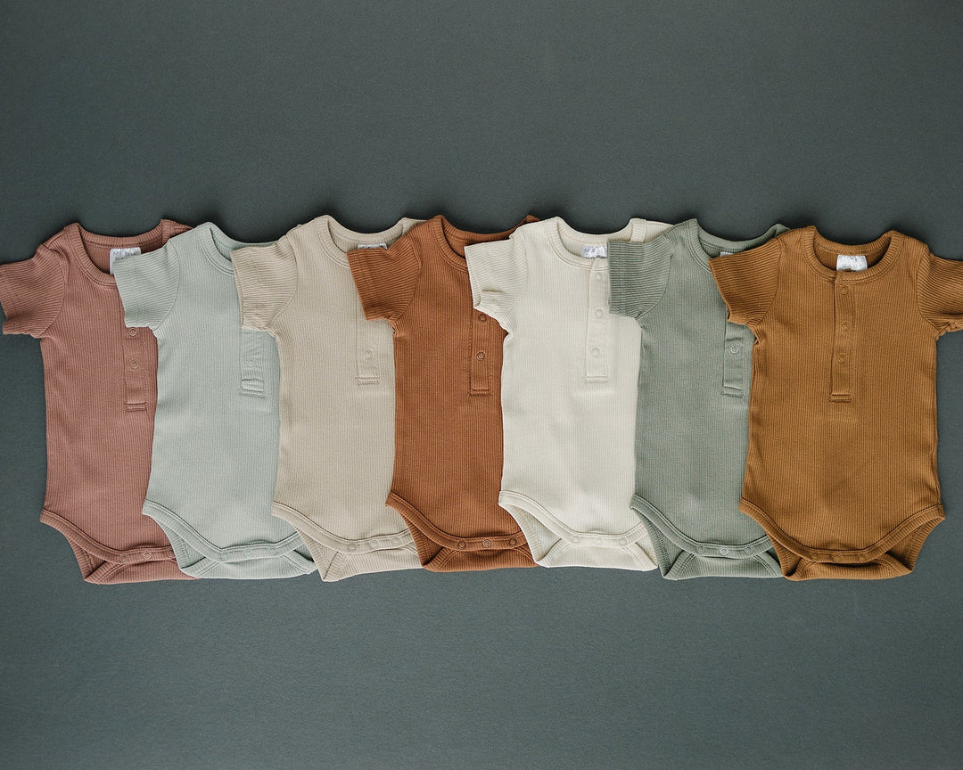 Sage Organic Cotton Ribbed Snap Bodysuit folded on a wooden shelf, an organic cotton ribbed baby bodysuit.