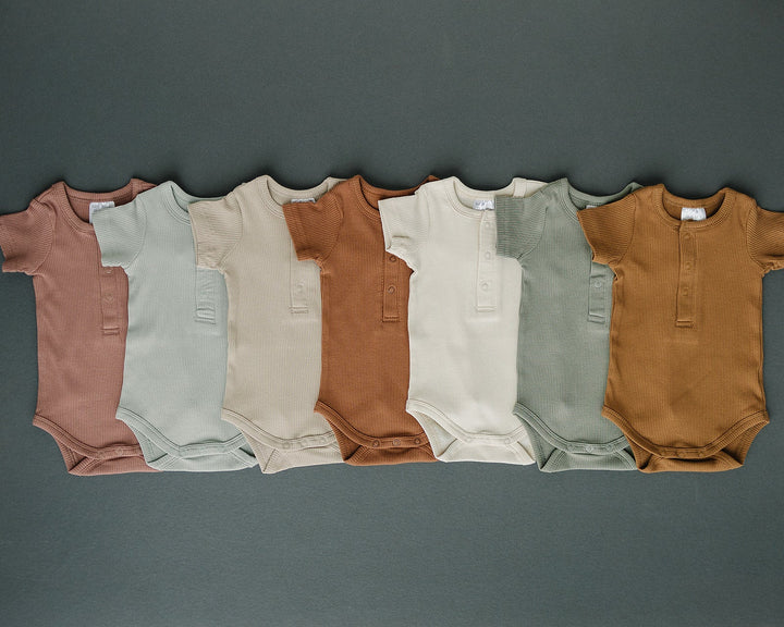 Sage Organic Cotton Ribbed Snap Bodysuit folded on a wooden shelf, an organic cotton ribbed baby bodysuit.