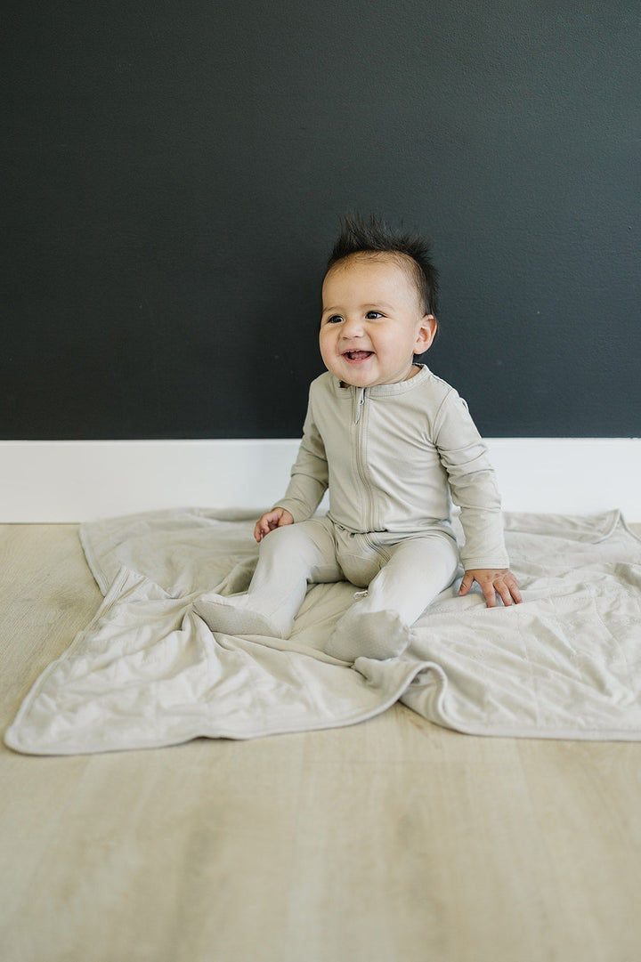 Worn by a baby on a play mat, the Mebie Baby Oatmeal Bamboo Footed Zipper.