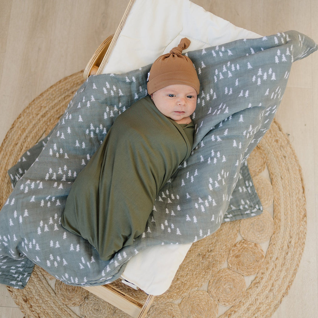 Olive Bamboo Stretch Swaddle from Mebie Baby, wrapped around a sleeping newborn.