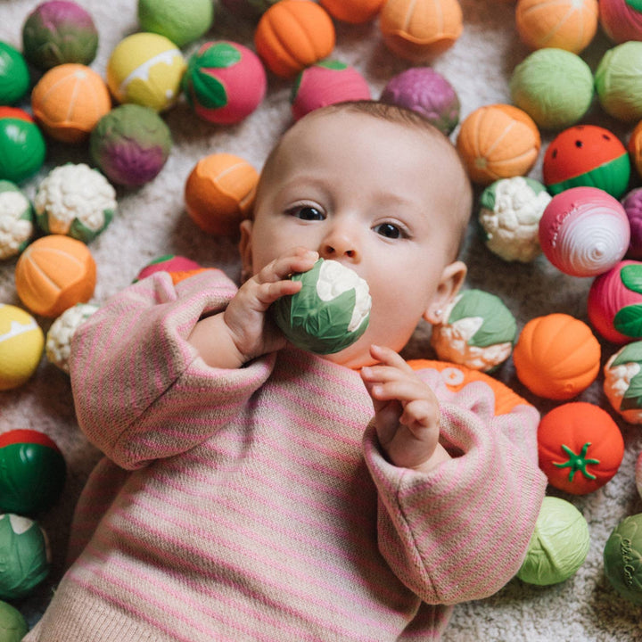 A baby surrounded by colorful sensory balls explores Oli & Carol Veggie Soup Baby Sensory Balls