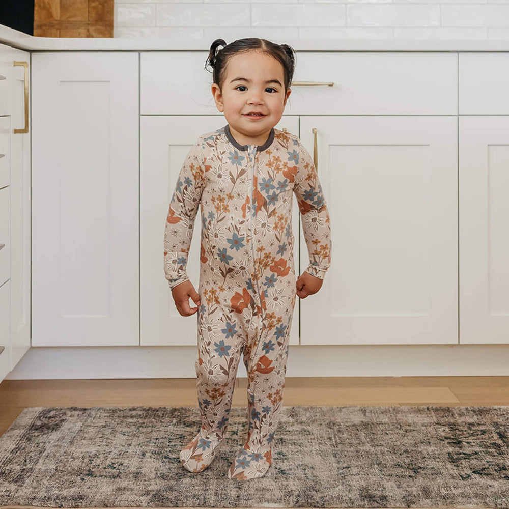 Toddler wearing Copper Pearl Eden zip-up footie pajamas standing in kitchen, soft bamboo sleepwear for toddlers and babies