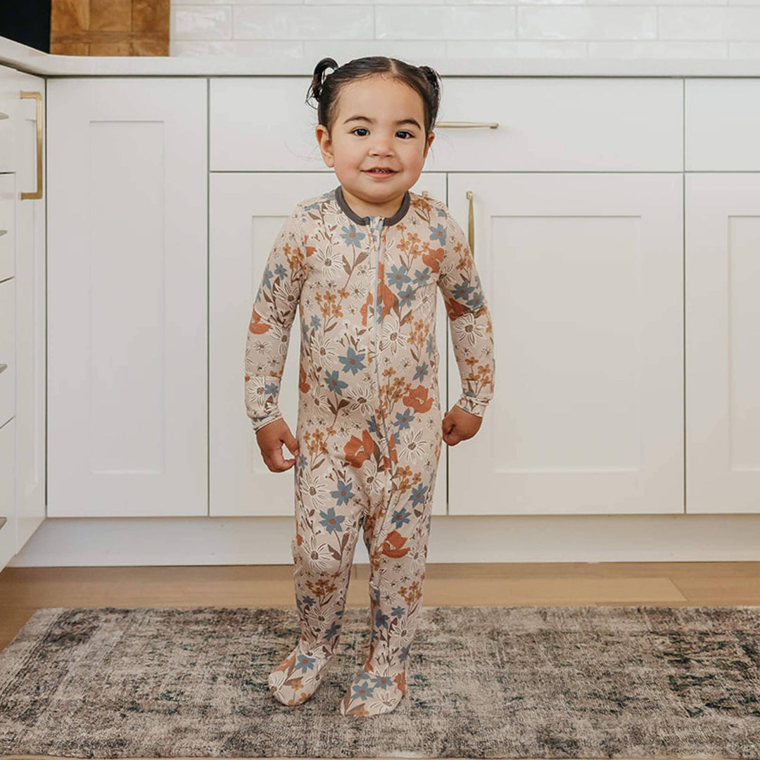 Toddler wearing Copper Pearl Eden zip-up footie pajamas standing in kitchen, soft bamboo sleepwear for toddlers and babies