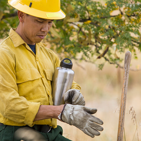 Firefighter using Klean Kanteen 64oz Wide Water Bottle in Black, metal and temperature controlled for reliable hydration.