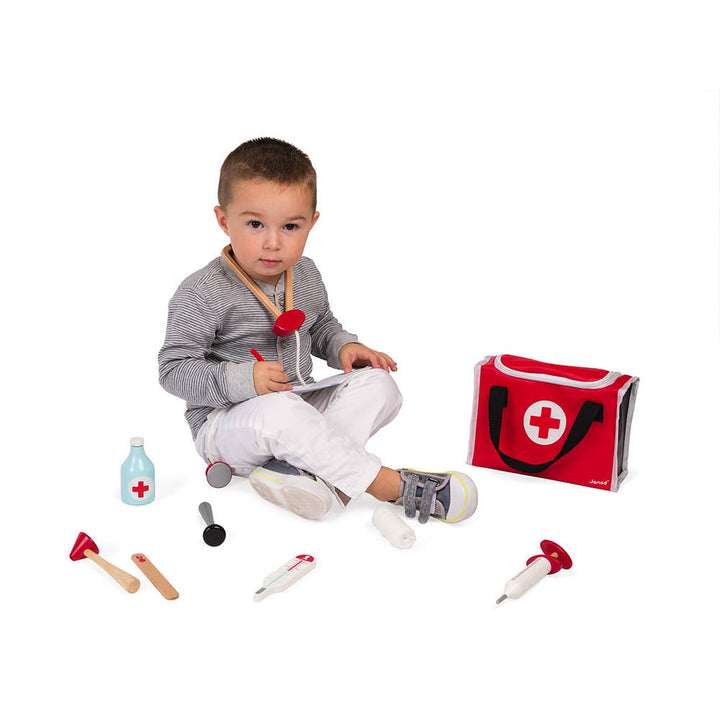 child playing with janod pretend play doctors toy set and sitting next to carrying bag