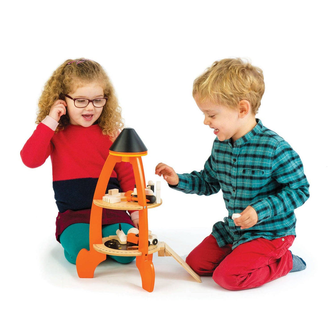 Two kids in cozy pajamas share pretend play time with the Cosmic Rocket Set from Tender Leaf Toys