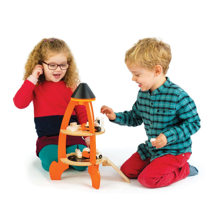 Two kids in cozy pajamas share pretend play time with the Cosmic Rocket Set from Tender Leaf Toys