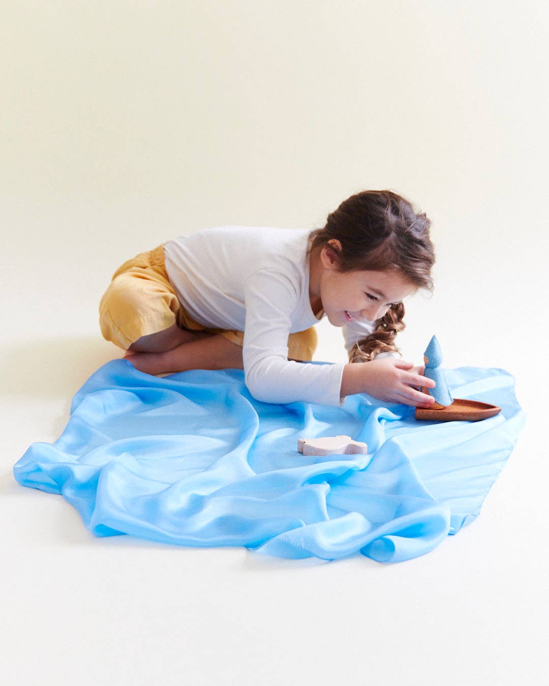 Child sitting and playing with a blue Sarah's Silks Solid Color Playsilk, a cherished plaything