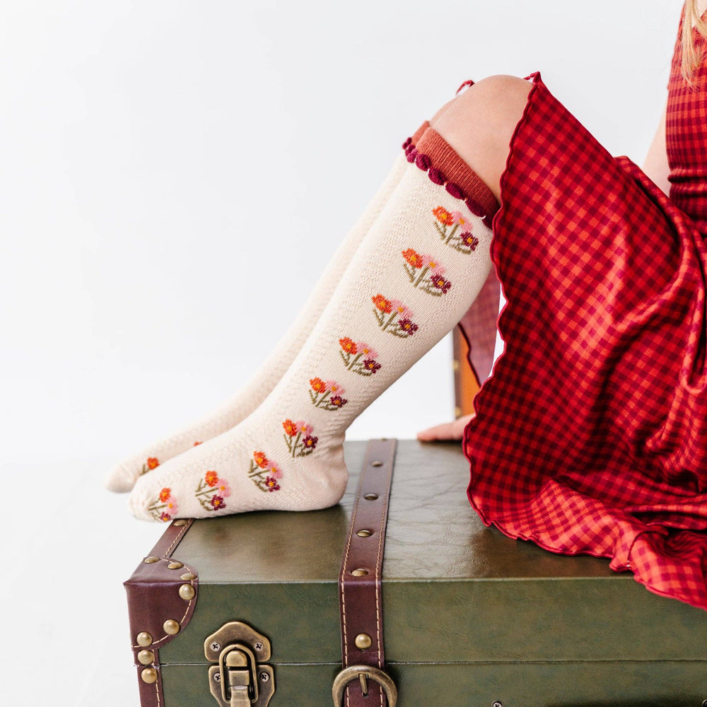 Baby wearing Little Stocking Co. Posie Knee Socks in Rust propped on a vintage suitcase, floral knee socks