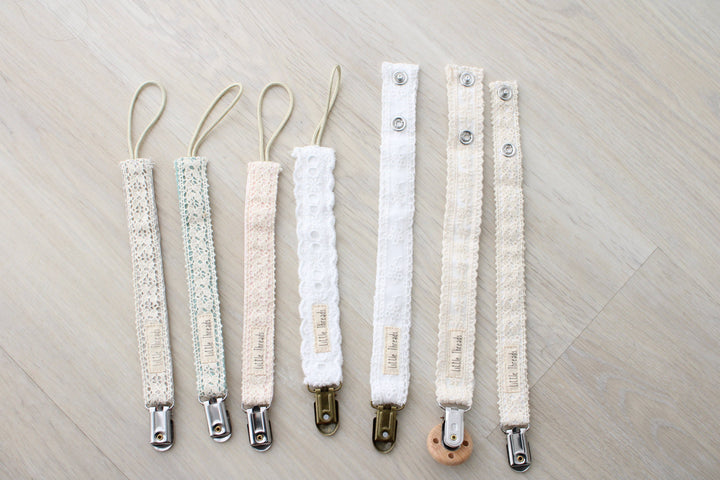 Little Threads pacifier clip collection lined up side by side, featuring the Ivory Floral Lace Pacifier Clip for infants