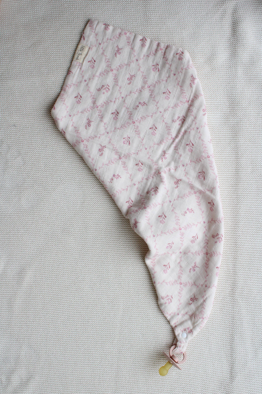 Mauve lattice lovey blanket by Little Threads draped diagonally with pacifier clip holder